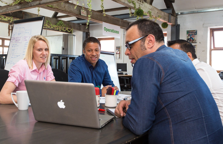Photograph of people sitting round a table looking at a laptop screen