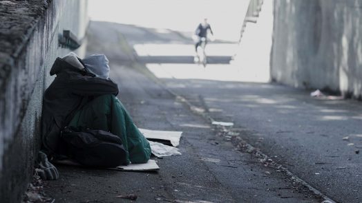 A photograph of a homeless person sitting on the street