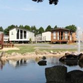 A photograph of static caravans sitting behind a lake and fountain