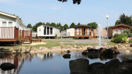A photograph of static caravans sitting behind a lake and fountain